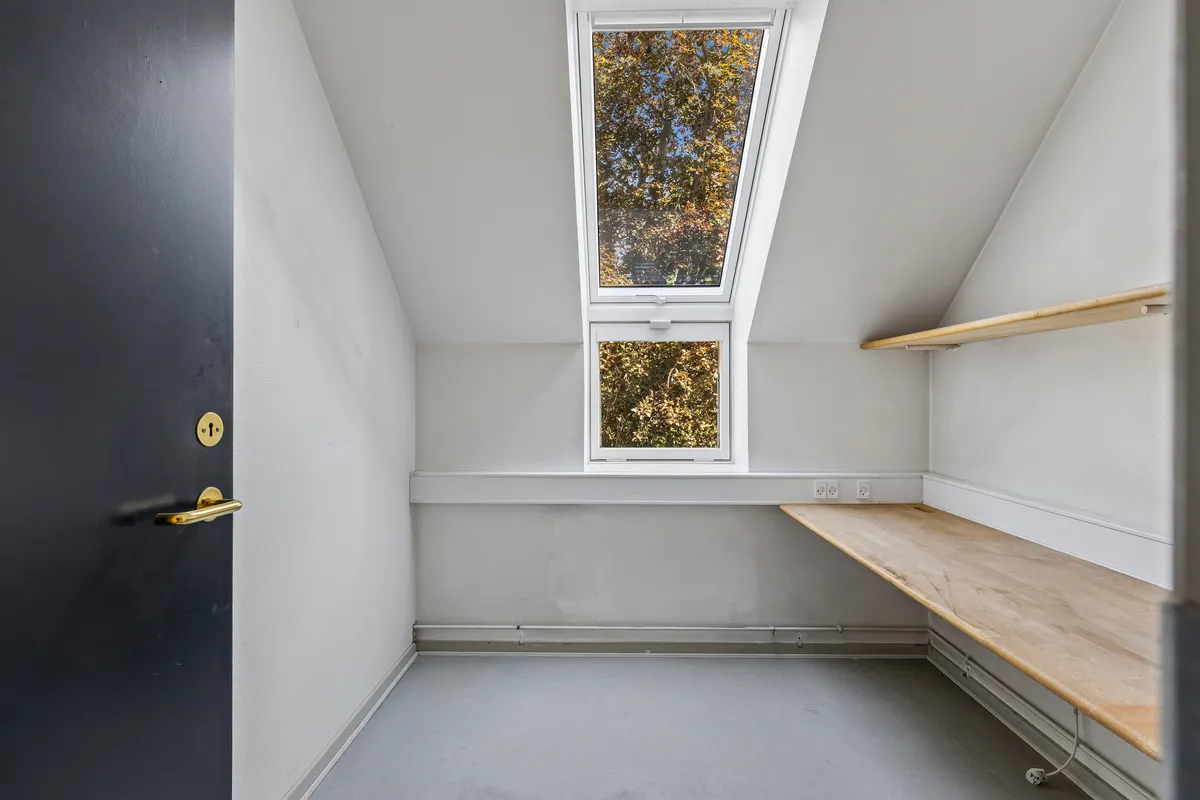 Et rum med to vinduer, en loftsvindu og en skrånende væg, hvor der er et brædt stel med to højttalere og en indbyggede stikkontakter