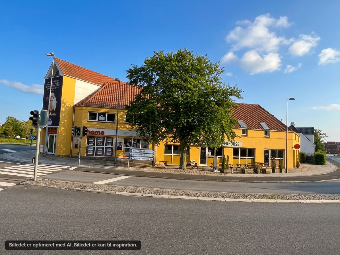Kontorby i Ballerup med gul facade og rødt tag, udstyret med vinduer, vejsidemøbler og parkerede biler.
