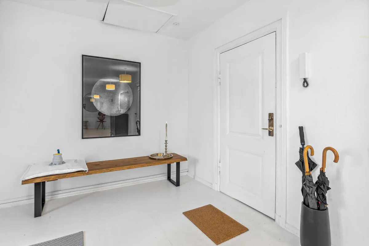 En elegant indgangsrum med lyse vægge, hvor der er en massiv brædt med bekvemme stole og en pragtfuld spejl med refleksioner
