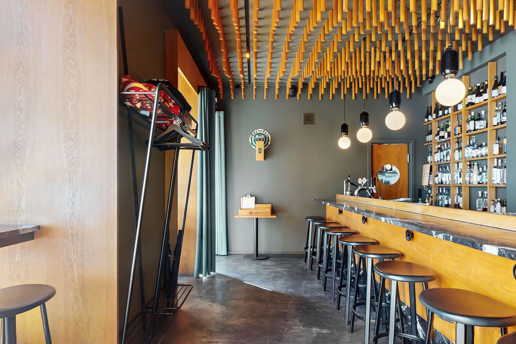 Indkøbsvogn i restaurant med støvler, barstole og ølflasker. Gul bar med marmor. Gule, lyse pærelamper. Gule loftsstave. Sorte og hvide vinflasker på hylder.