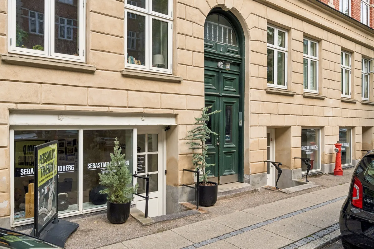 Kontor til leje på Roarsvej 6 med lyse vinduer og grønne døre. Foran er slanke søjler, og der står to små plantepotter på fortovet.