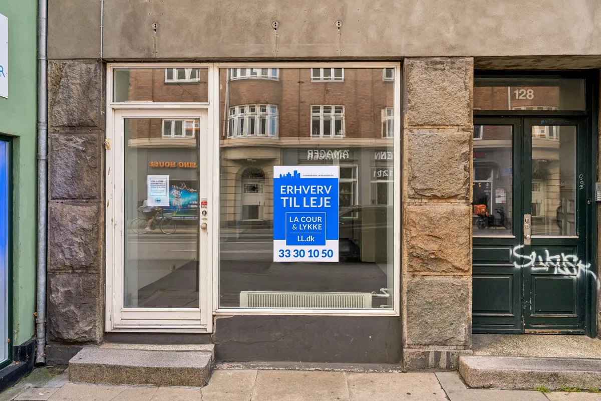 Butikstilbud på Amagerbrogade 128 i København S med skilt og glasdør, udvendig refleksion af cyklist og bil, indvendig varmeapparat og grafisk annonce