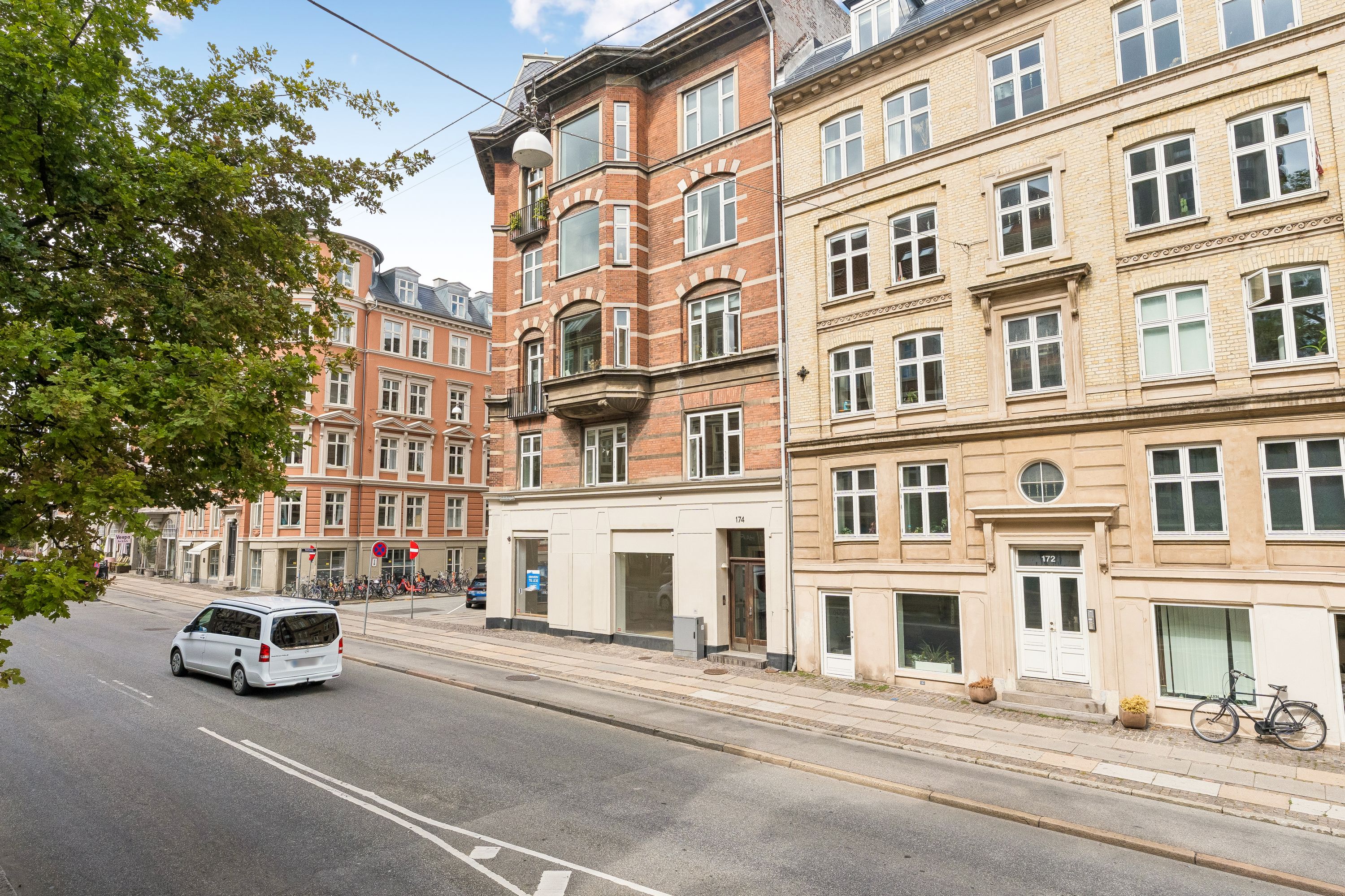 Butik på hjørnet af Vesterbrogade 174 i Frederiksberg. En hvid Mercedes Vito kører langs gaden. Der er en cykel udenfor døren. Bygningen har røde mursten og mange vinduer.
