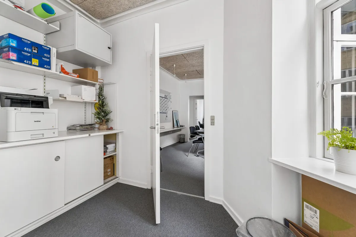 Kontor med moderne hvidt møbel og printer, indvendigt kontorruum med gulv og hvid væg samt plante og skrivebord med stol og computer