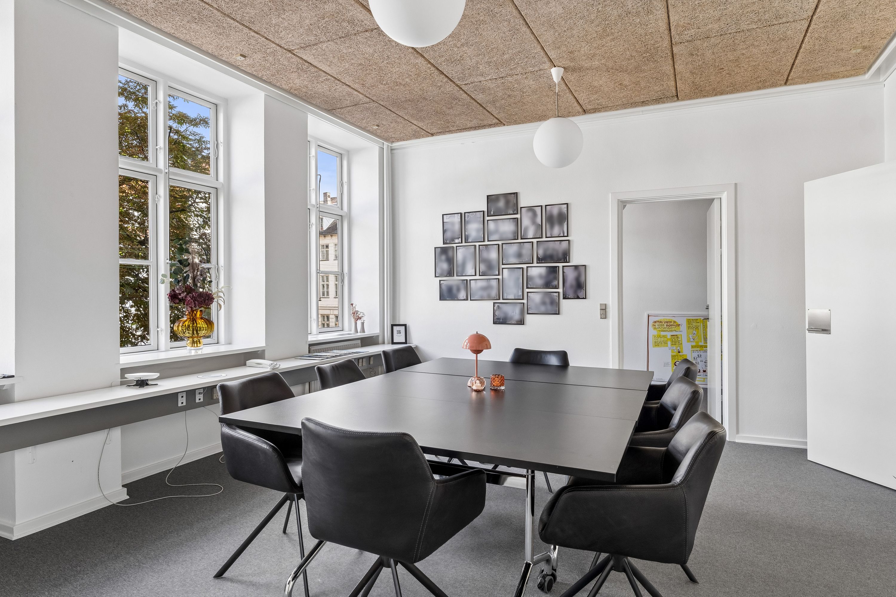 Moderne kontor med møbler og lyse vinduer. Bord med lyse lamper og lyse buede stolpe. Foto på væggen.