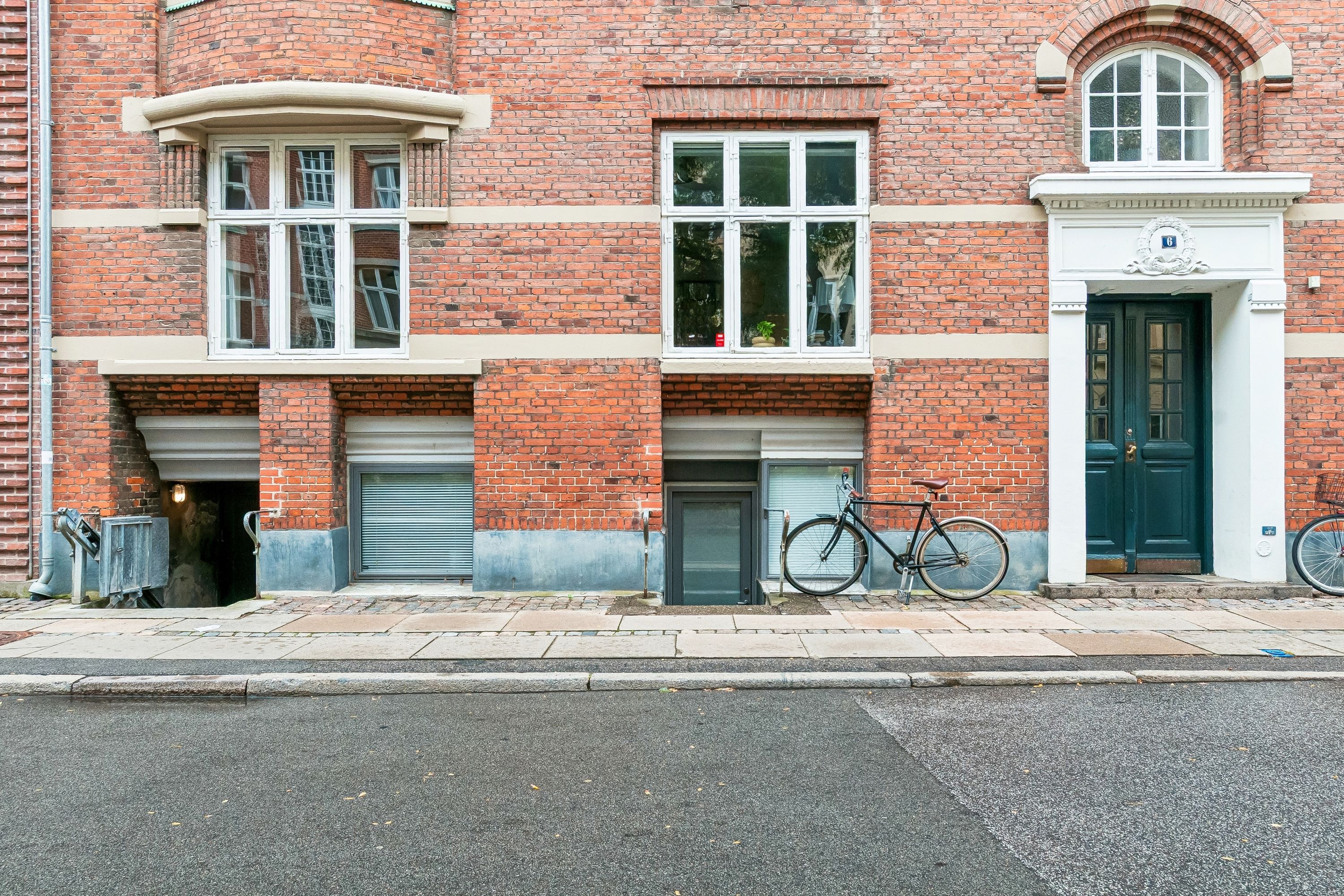 To lejligheder med store vinduer og en stående cykel og et stel foran døren på en husside i røde mursten med et nummer 6 i øverste hjørne