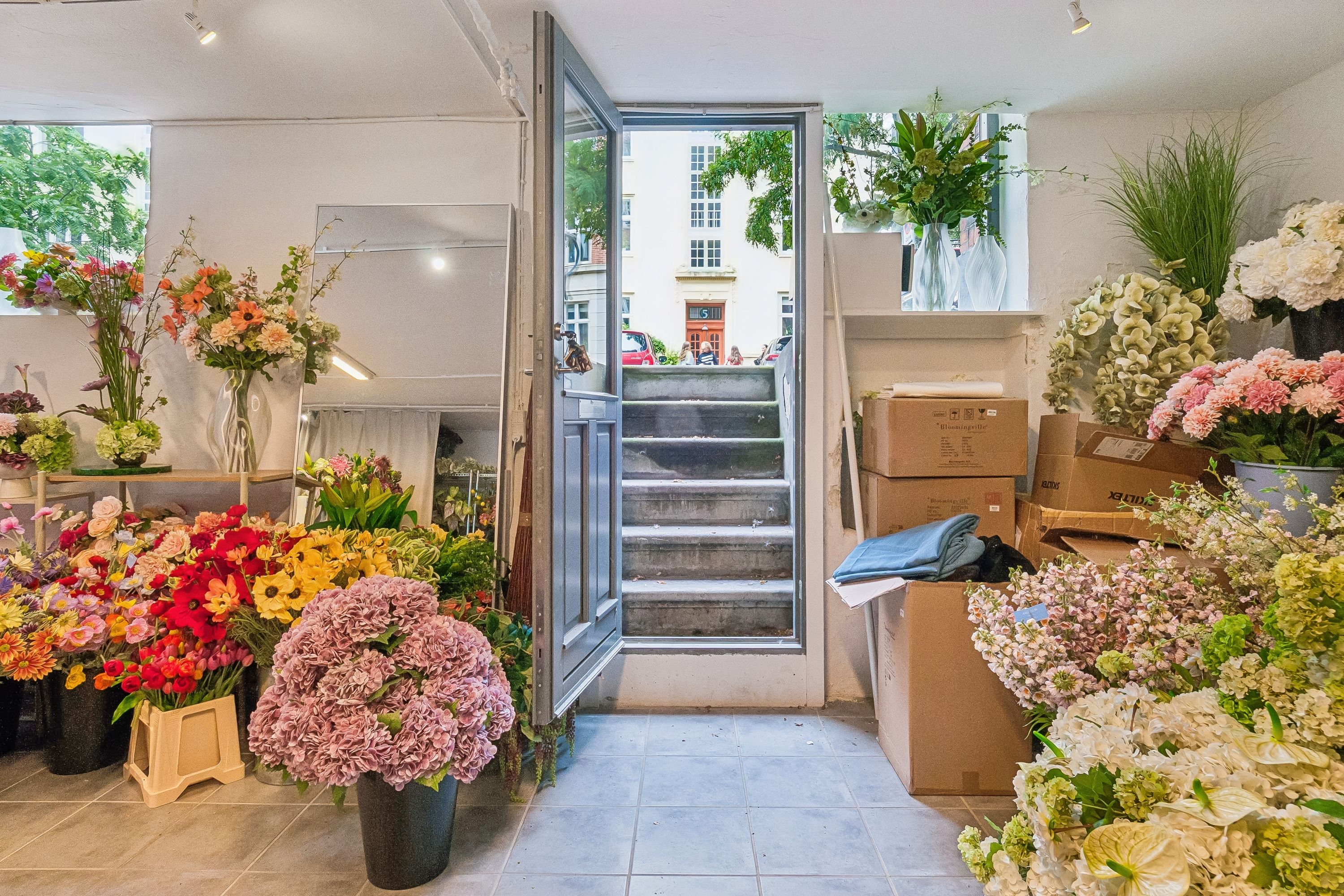 Blomsterbutik med udskæring af blomster og plante i forskellige farver og størrelser samt flere kasser og blomsterpotter i rummet
