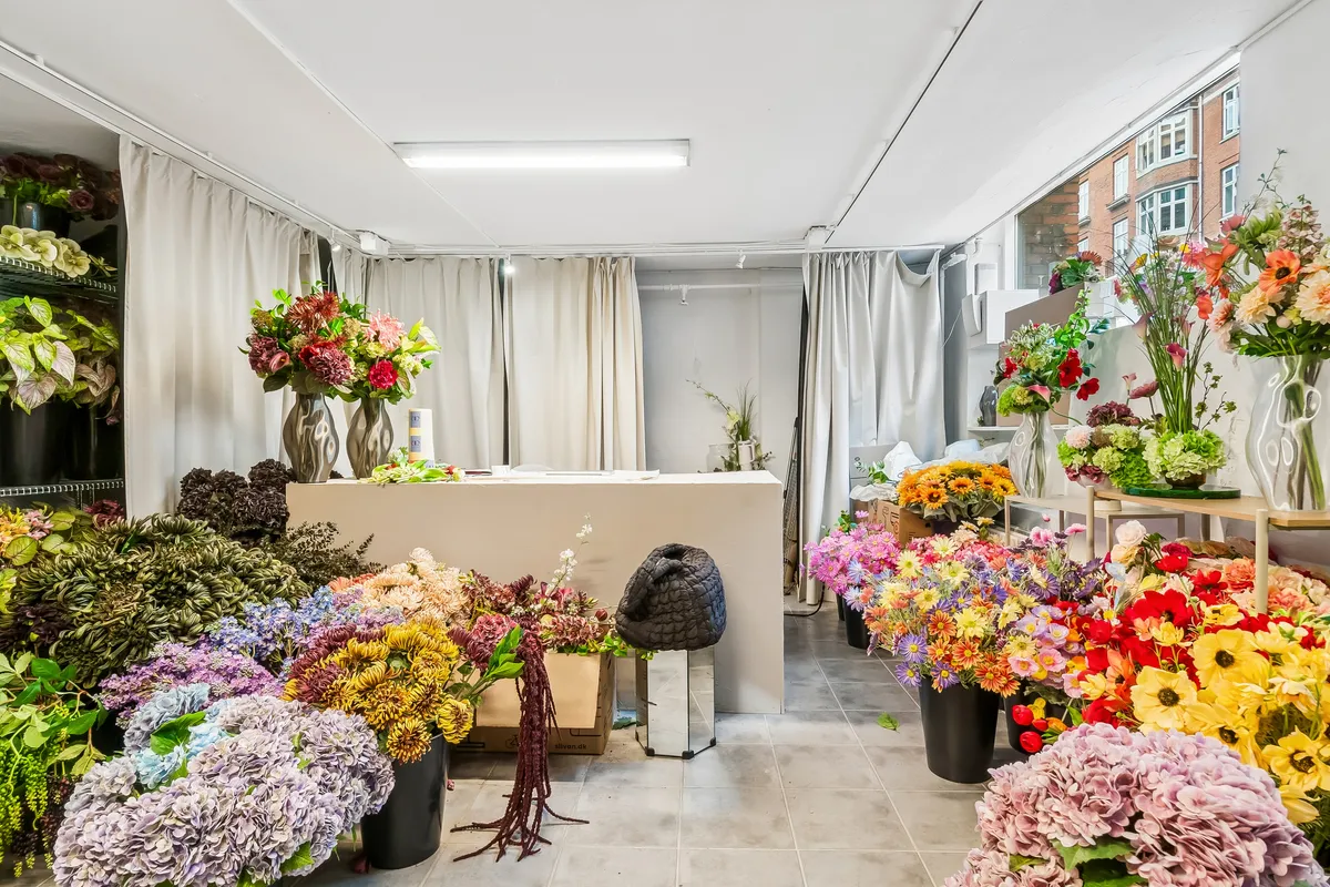 Blomsterbutik med store blomster i forskellige farver og sorter, hylder med blomster, væggardiser, skovl og stående lysekroner