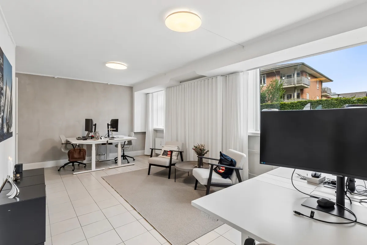 Kontor med skrivebord, stole, monitor og møbler samt et udsigtsvindue til gaden