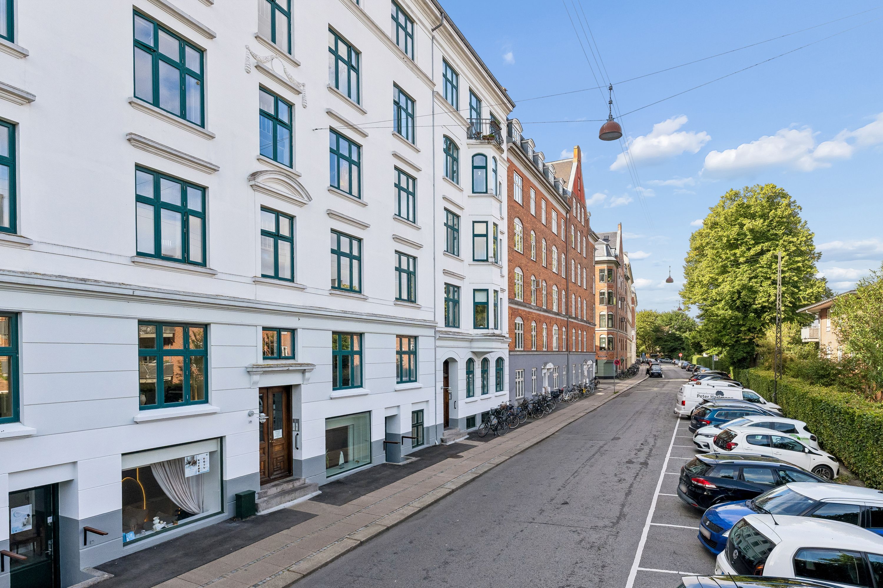 Kontorbyggeri med lyseruder, parkerede biler, grønne buske og elektriske kabler på en fredelig vej på Østerbro i København