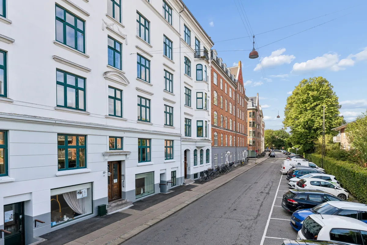 Kontorbyggeri med lyseruder, parkerede biler, grønne buske og elektriske kabler på en fredelig vej på Østerbro i København