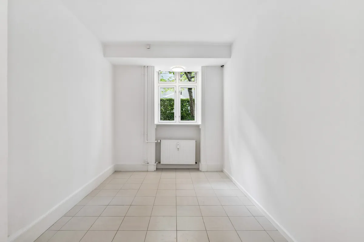 Et lyst og rummeligt kontor med hvide vægge og en stor, glasklædt vinduesåbning mod en gårdsplads.