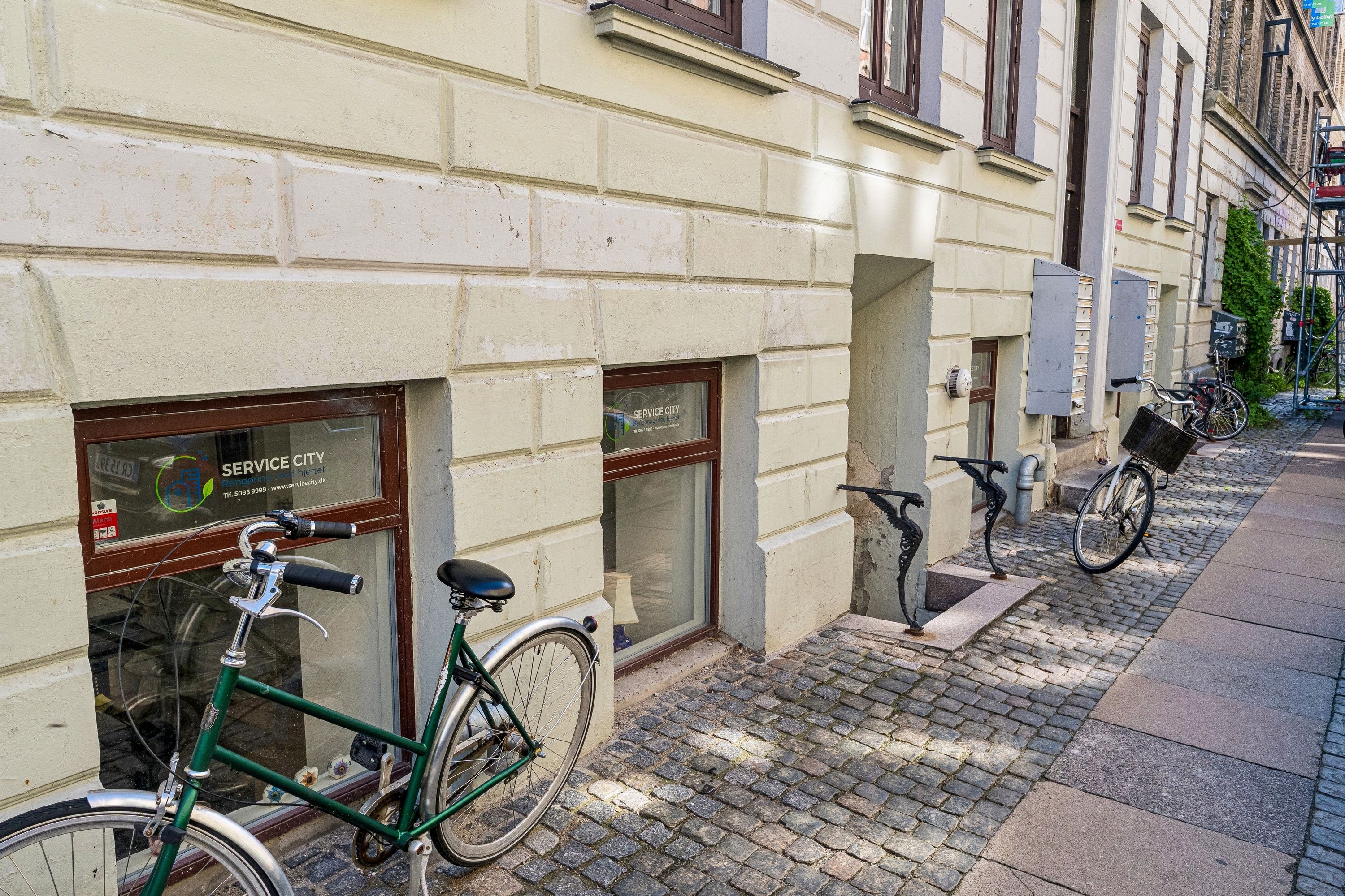 Grøn cykel parkeret udenfor en hvid murstensbygning med servicecity butik og servicebygninger, der går langs siden af gaden