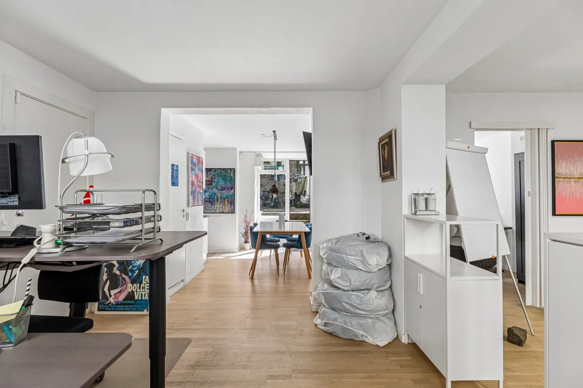 Kontor med høj kvalitet i høj kælder. Rummelig stue med højt loft og masser af lys. Værelse med skrivebord, stol og skærm. Malerier på væggen og møbler i moderne stil.