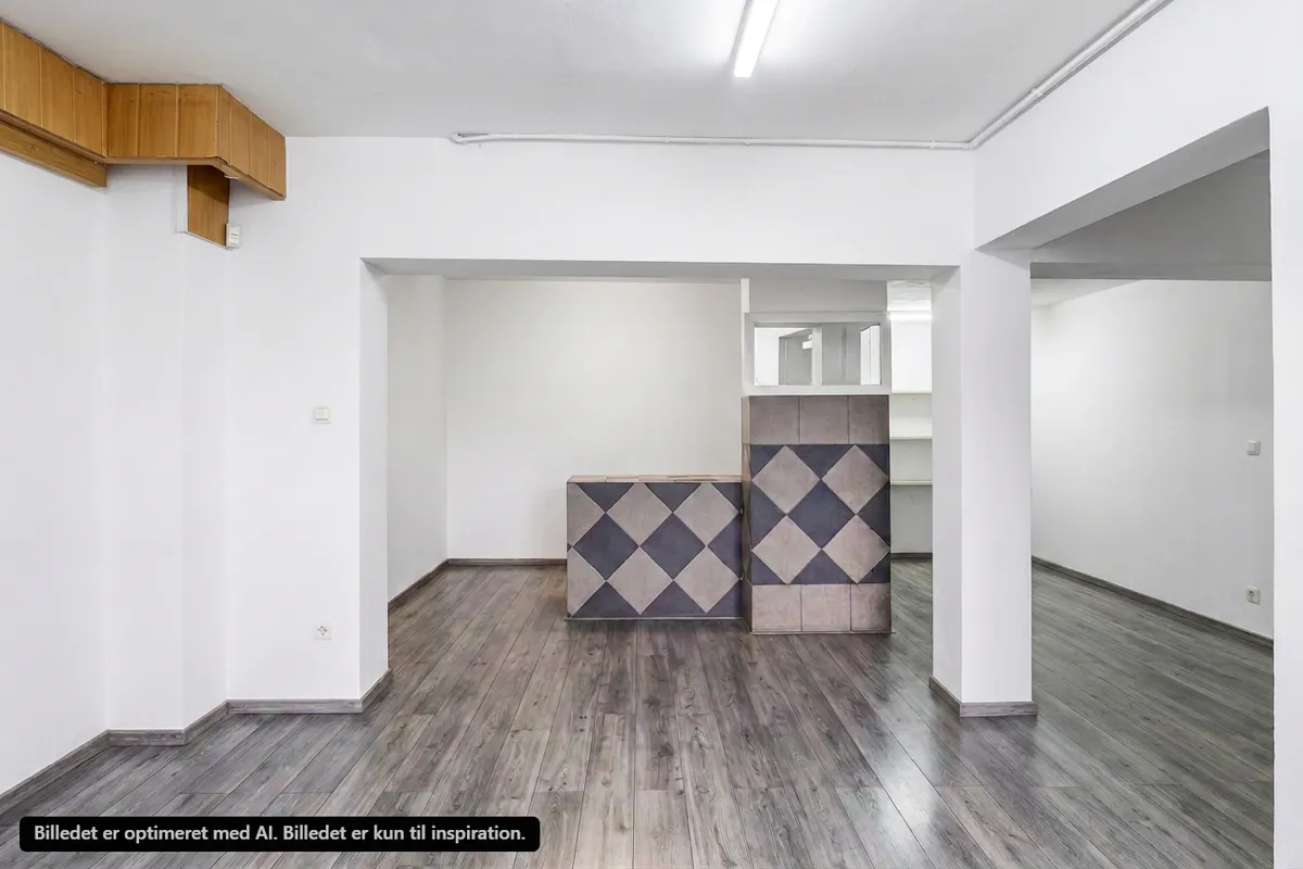 Store tommede butikslokaler med trægulv og hvide vægge, møbler og tekstiler er manglende. Hjørner og loft er tørre og lette. En træhylde er placeret mod højre.