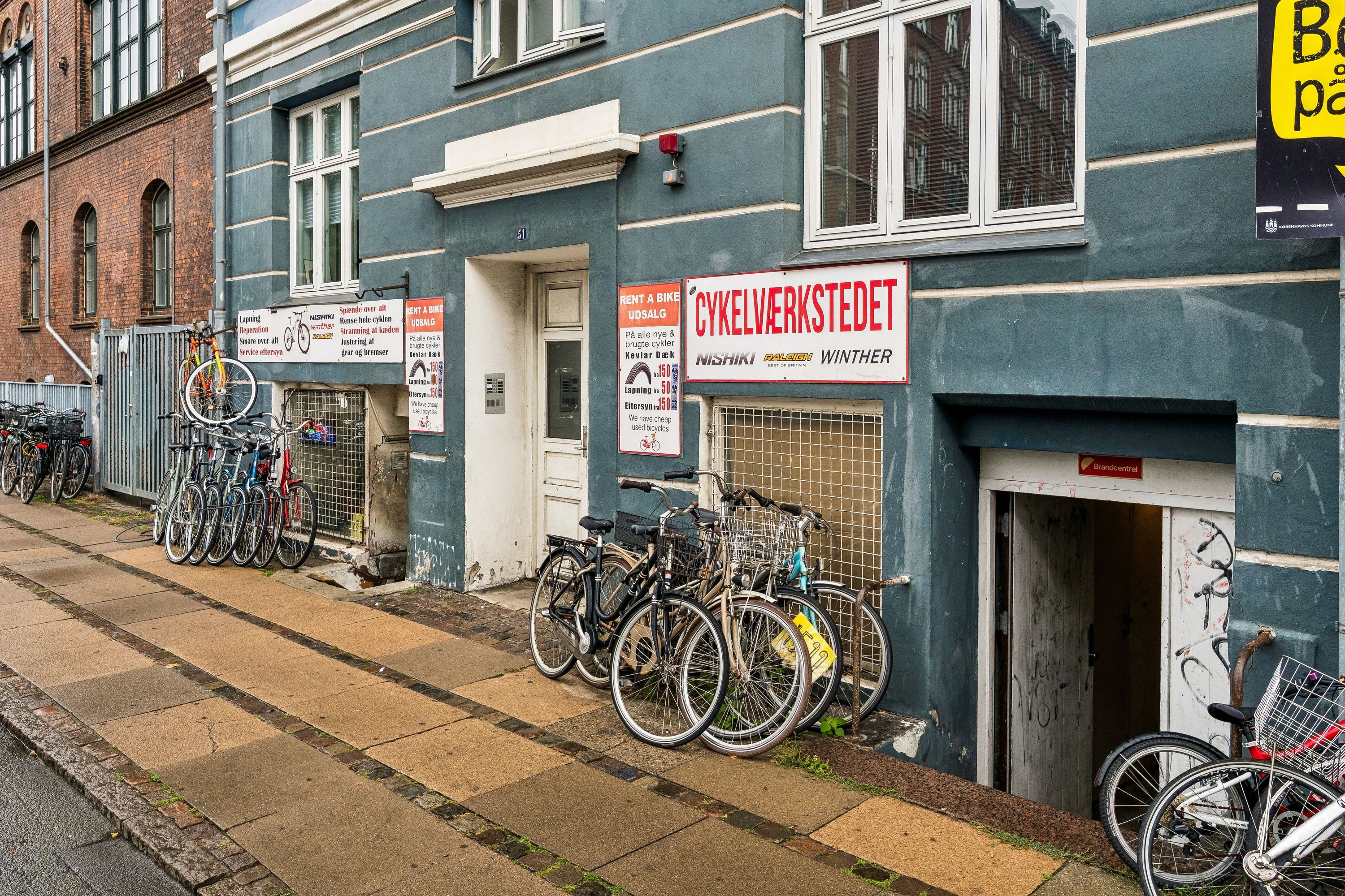 Lejlighed med butik til leje på Enghavevej 51 med plakater om cykeludlejning og reparationer samt flere cykler parkeret udenfor