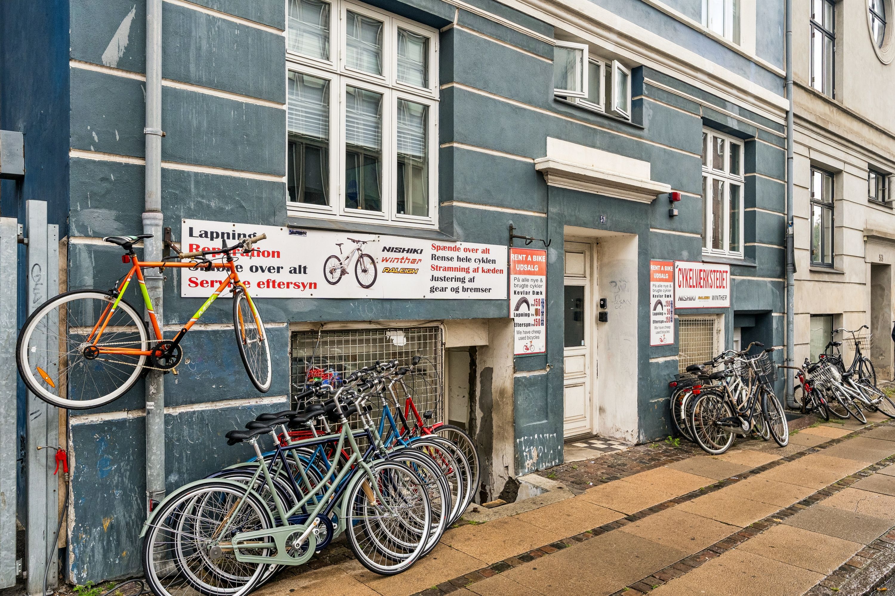 Leje cykelforretning på Enghavevej 51, 1674 København V. Rent cykel på engelsk. Forskellige farvede cykler parkeret udenfor. Cykler og tilbehør til leje og salg.