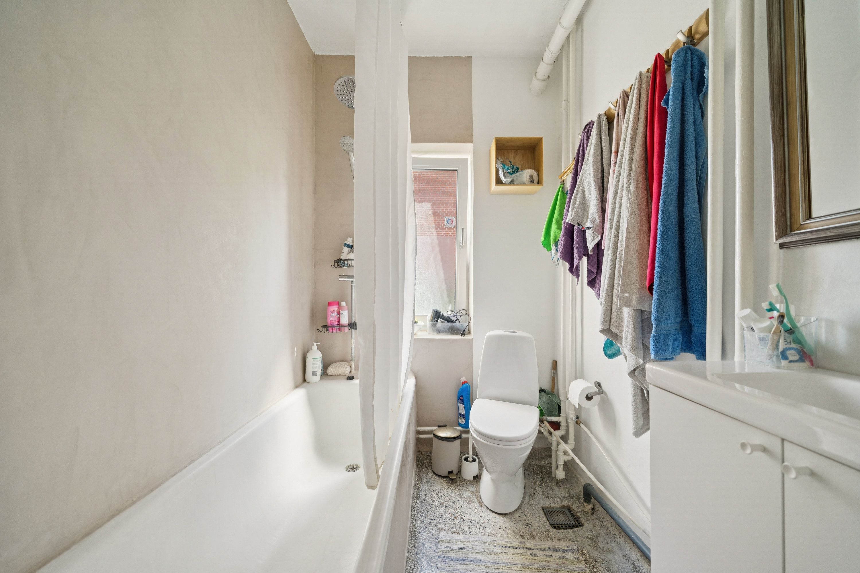 En ren og veludstyret badeværelse med hvidt badekar og toilet samt håndklæder og rengøringsprodukter