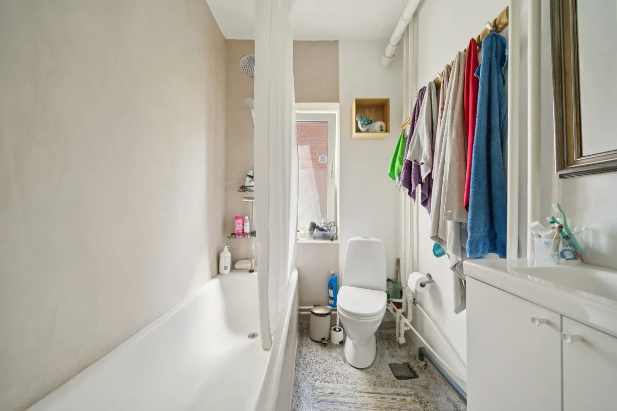 En ren og veludstyret badeværelse med hvidt badekar og toilet samt håndklæder og rengøringsprodukter