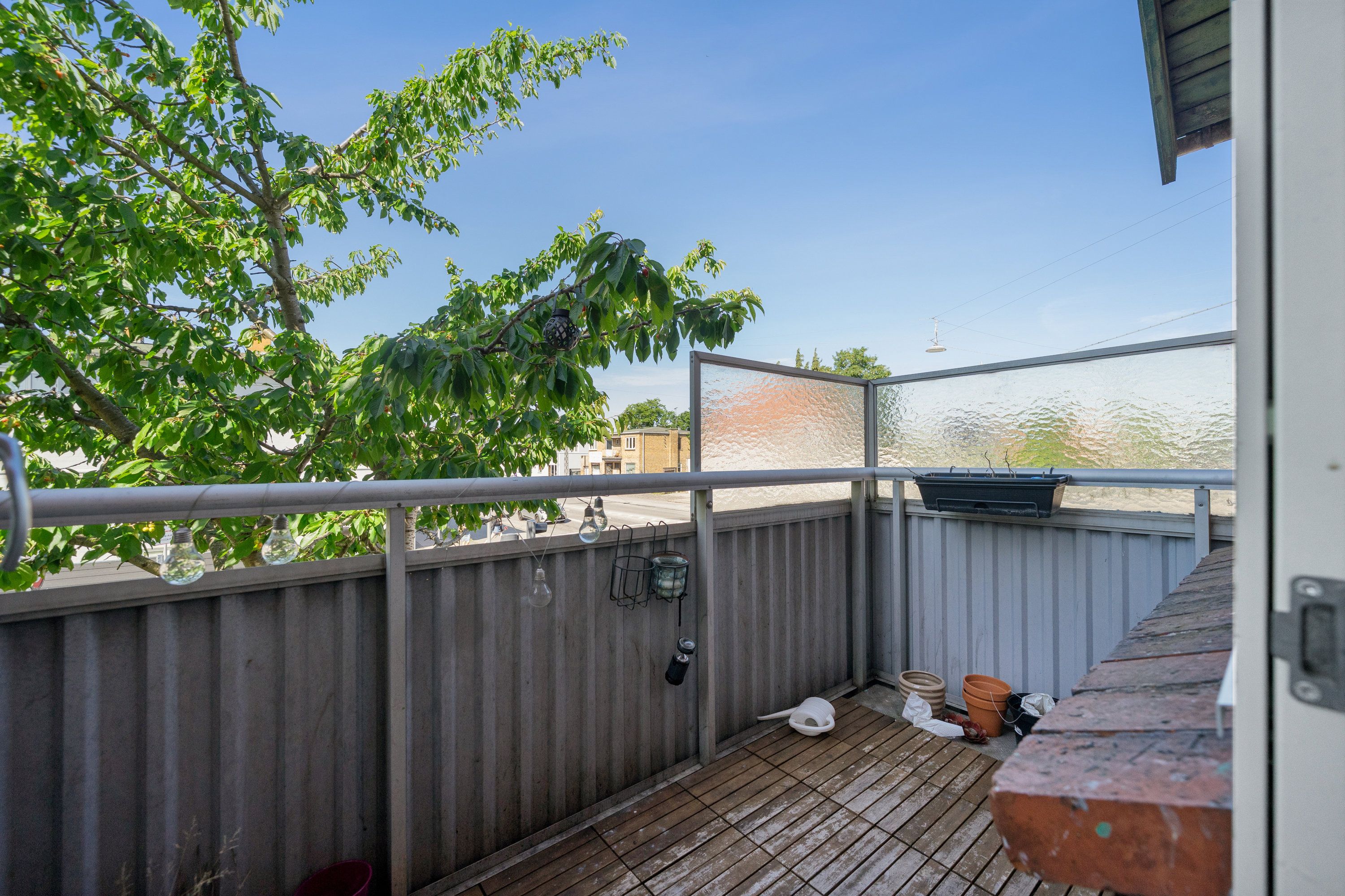 Balkon med trægulv, glaspanel, brædder, potteplante, lyseperler, søjler, træ, gulv og åben dør med metalhåndtag