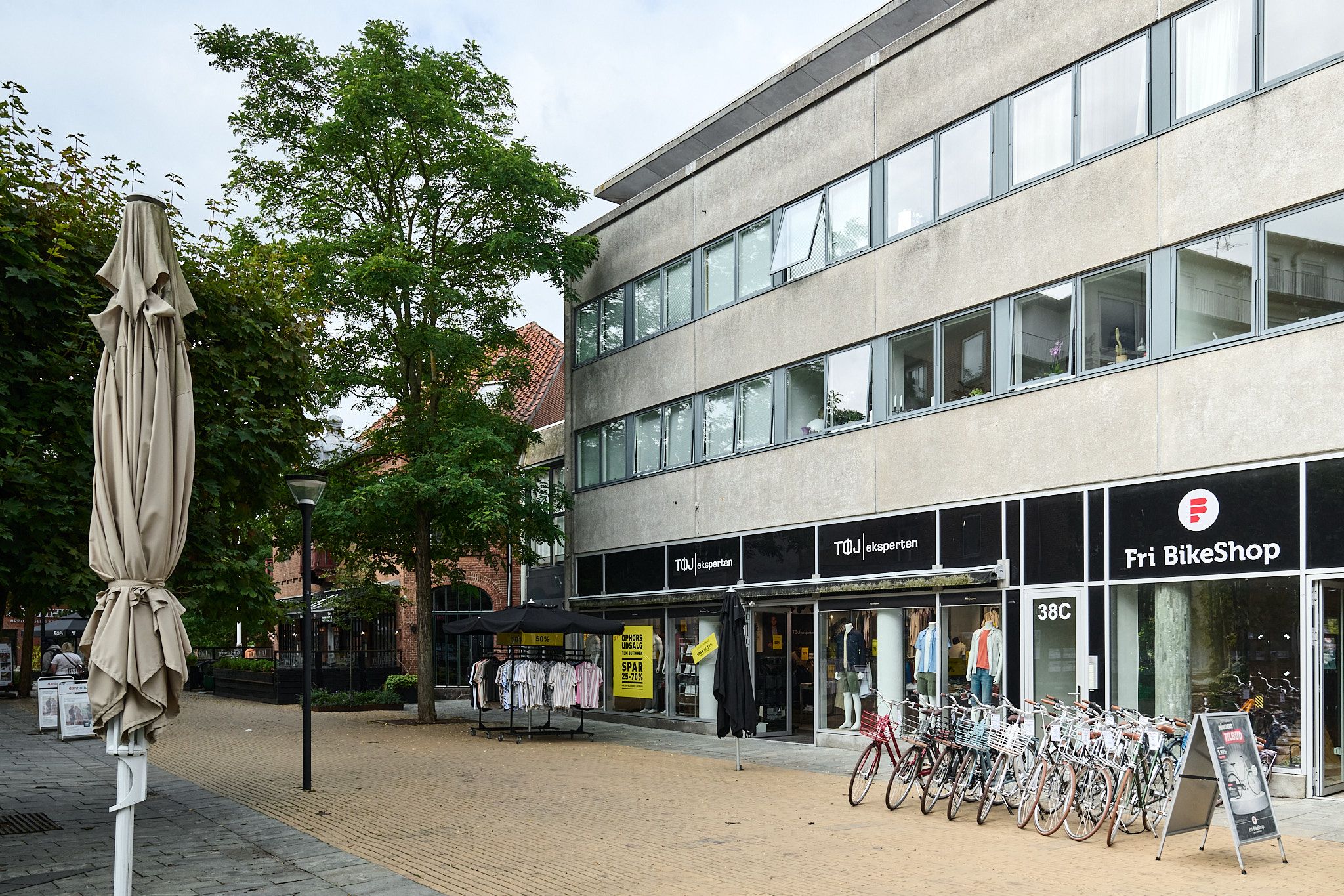 Butik med cykler udenfor og indstillinger og tøj indenfor, samt en træplantning og en paraply.