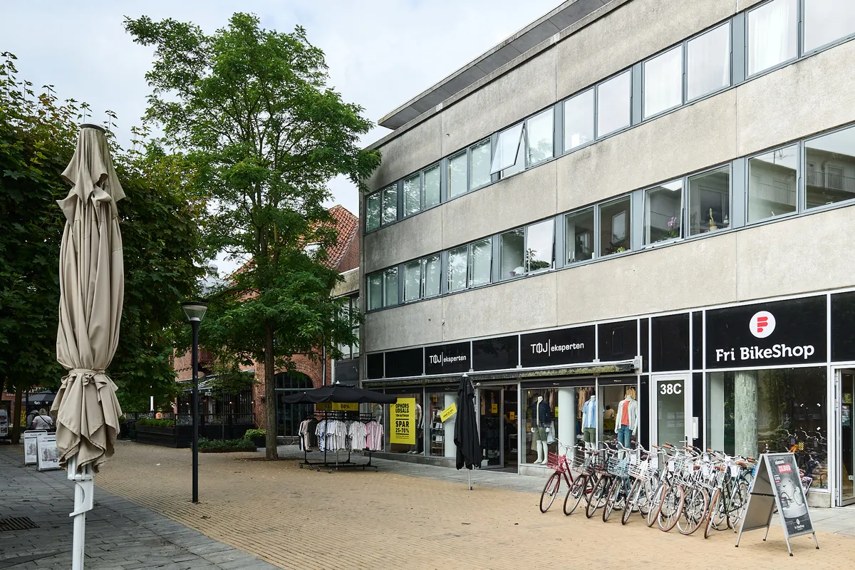 Butik med cykler udenfor og indstillinger og tøj indenfor, samt en træplantning og en paraply.