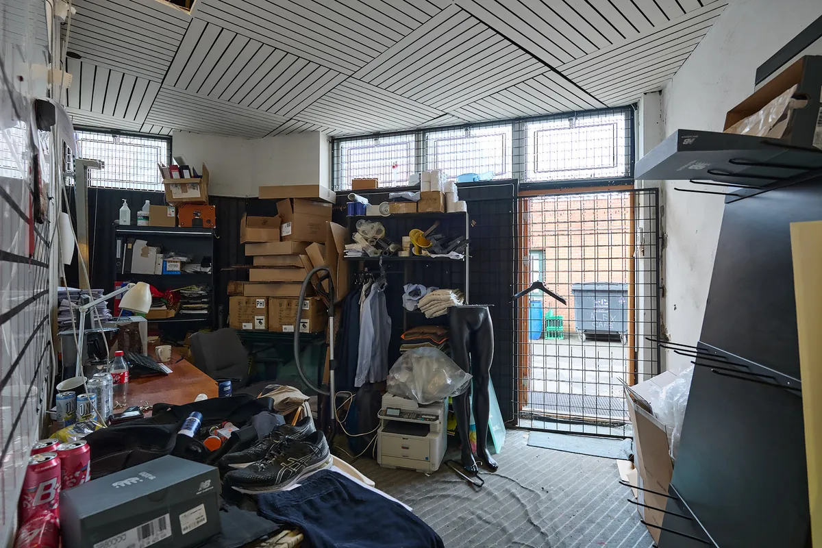 Rummeligt og veludstyret rum med skraldespande, printer, søjler, papkasser, sko og møbler i udstyret.