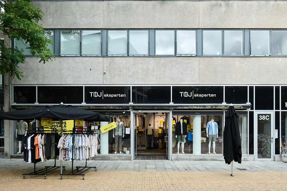 Butik med tøj i Birkerød. Tøjbutik med mærke TOM. Tøj på udstilling og udsalg. Sort paraply og tøjstativ udenfor.