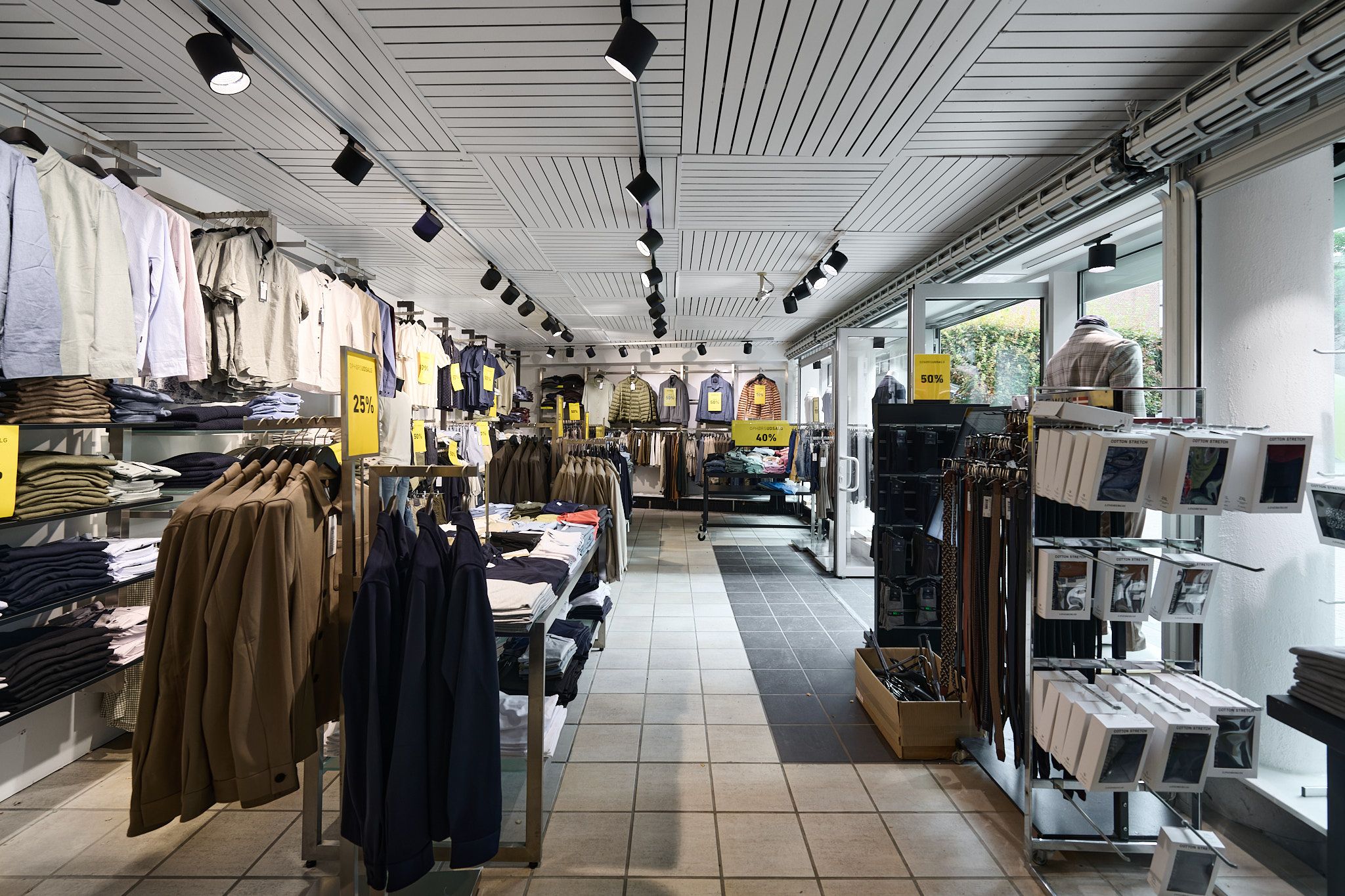 Inde i en ren og velorganiseret butik er der tøj, bælter og smykker. Alle produkter er udstillet på hylder og på hængegrej. Lyser hænger fra loftet, og der er rabatter på tøjet