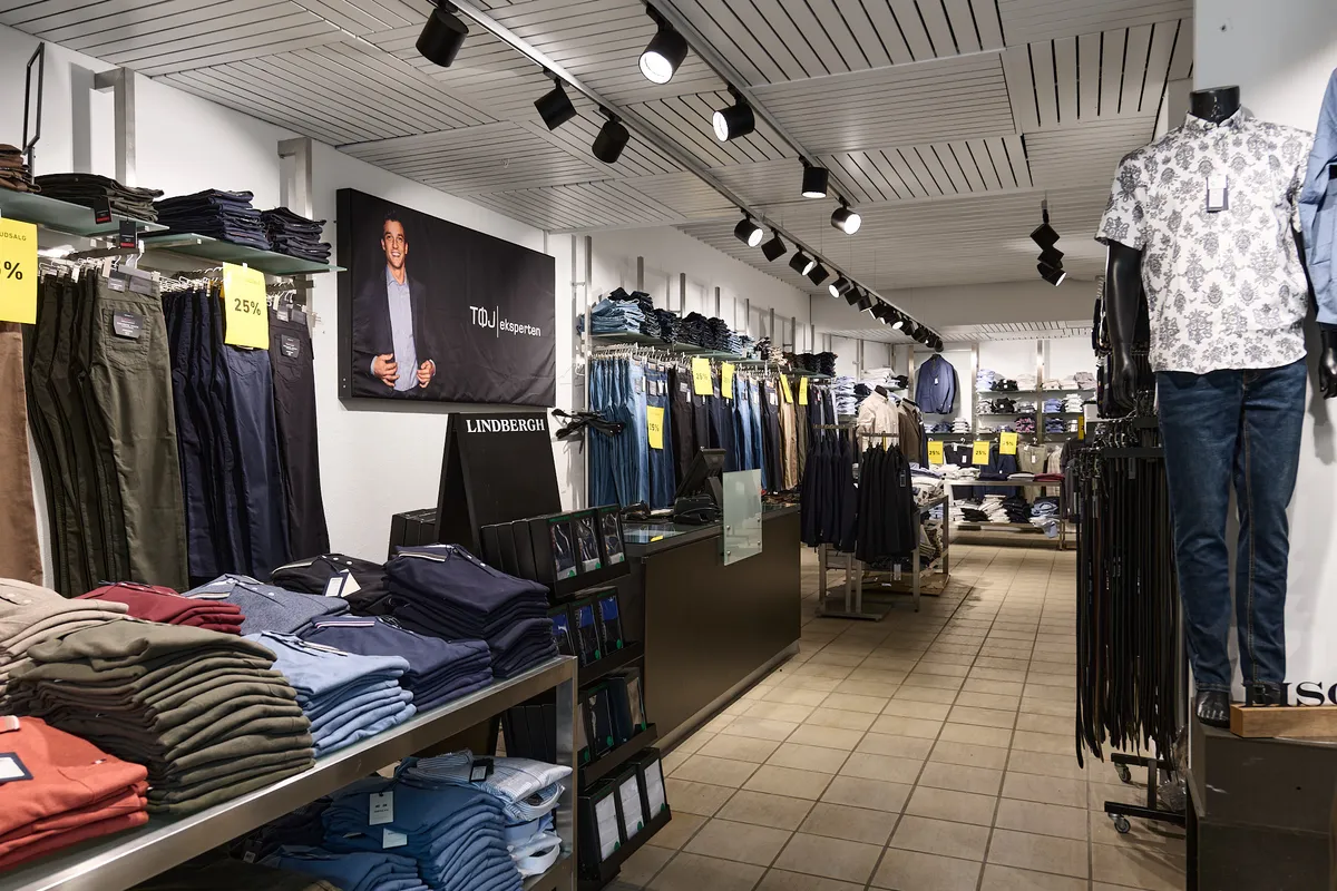 Butik med tøj, jeans og skjorter i et eksklusivt mærke, Lindberg. Prisskilte med 25% rabat, og mænd i blazer på væggen.