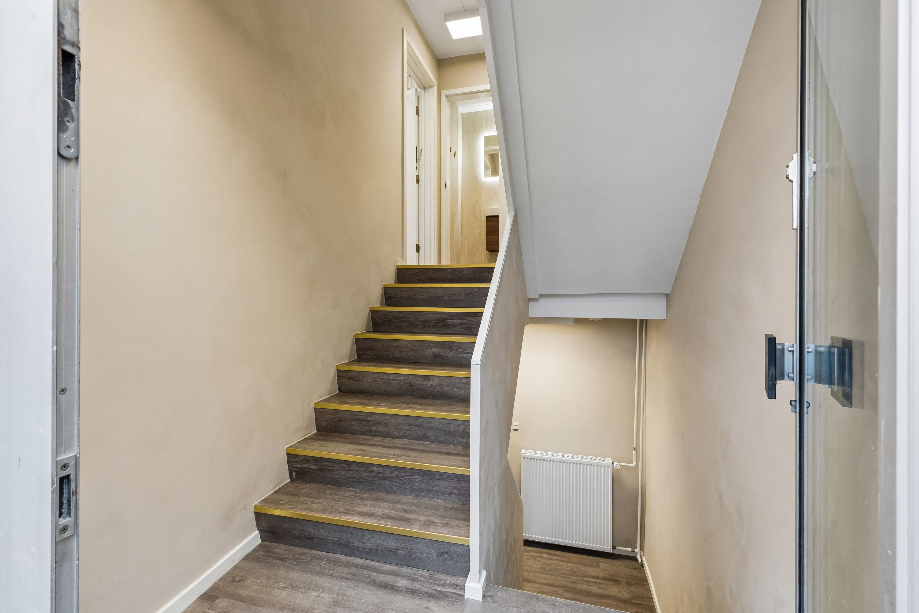 Kontor til leje med moderne faciliteter, der kombinerer nye gulve, hvide vægge og en luksuriøs hvid radiator. De lyse, træbelæggede trapper fører op til første sal