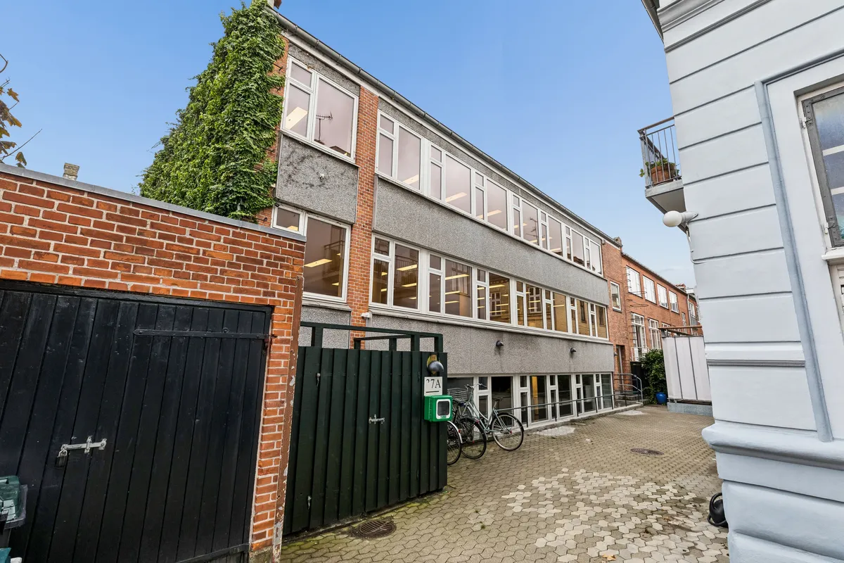 Kontor til leje på Frederiksberg. Moderne kontorlejemål med glasvinduer og skrånende tag. Grønne stiger og en terrasse med potteplanter. To cykler parkeret foran.