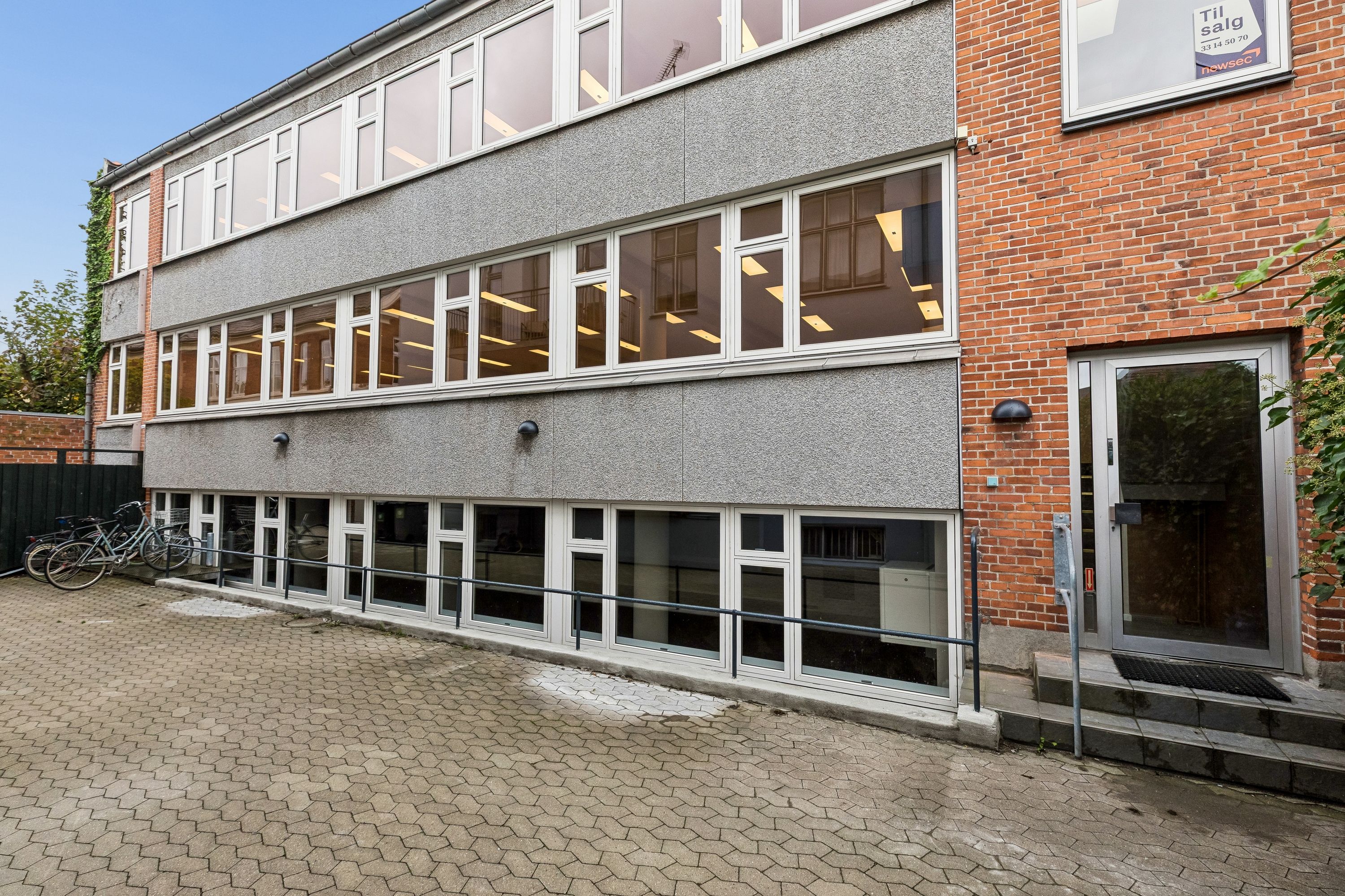Kontorbyggeri med glasvinduer og røde mursten samt en glasdør og en søjle ved siden af