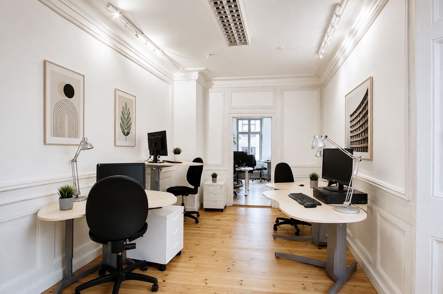 Kontor med højt loft og lyse vægge med smukke lysekroner. Moderne, hvide møbler og computere samt lyse loftslampe. Maleri på væggen og lyse trægulve.