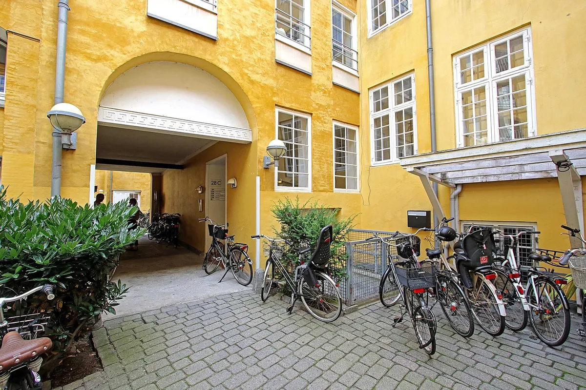 Flere hollandske cykler parkeret ved et gult bygningslejemål i Latinerkvarter i København med træflise og søjler ved indgangen