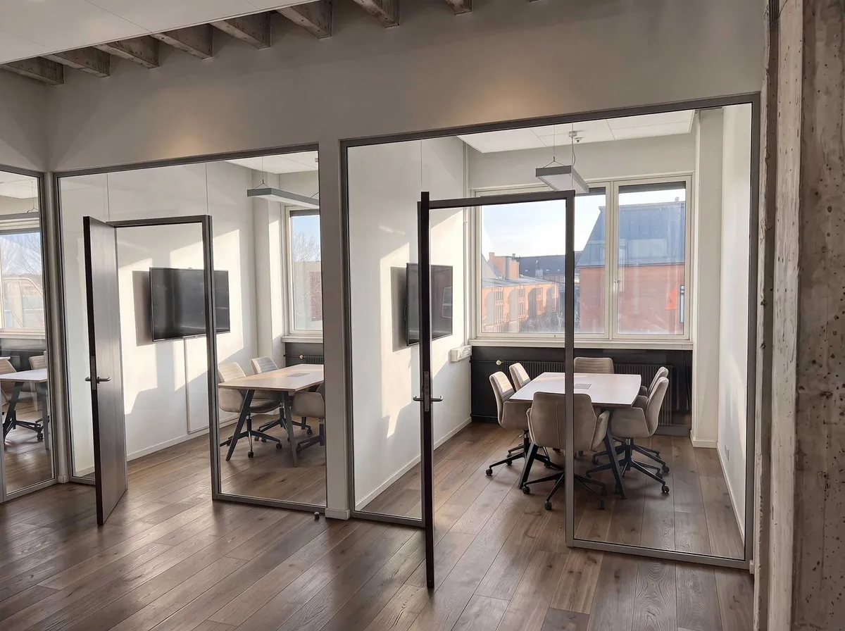 Moderne kontor med industridesign, højloftede lokaler, hvide vægge, glasdøre, højtalere, lyse trægulve, moderne møbler, store vinduer med udsigt til byen, fleksible kontorfaciliteter