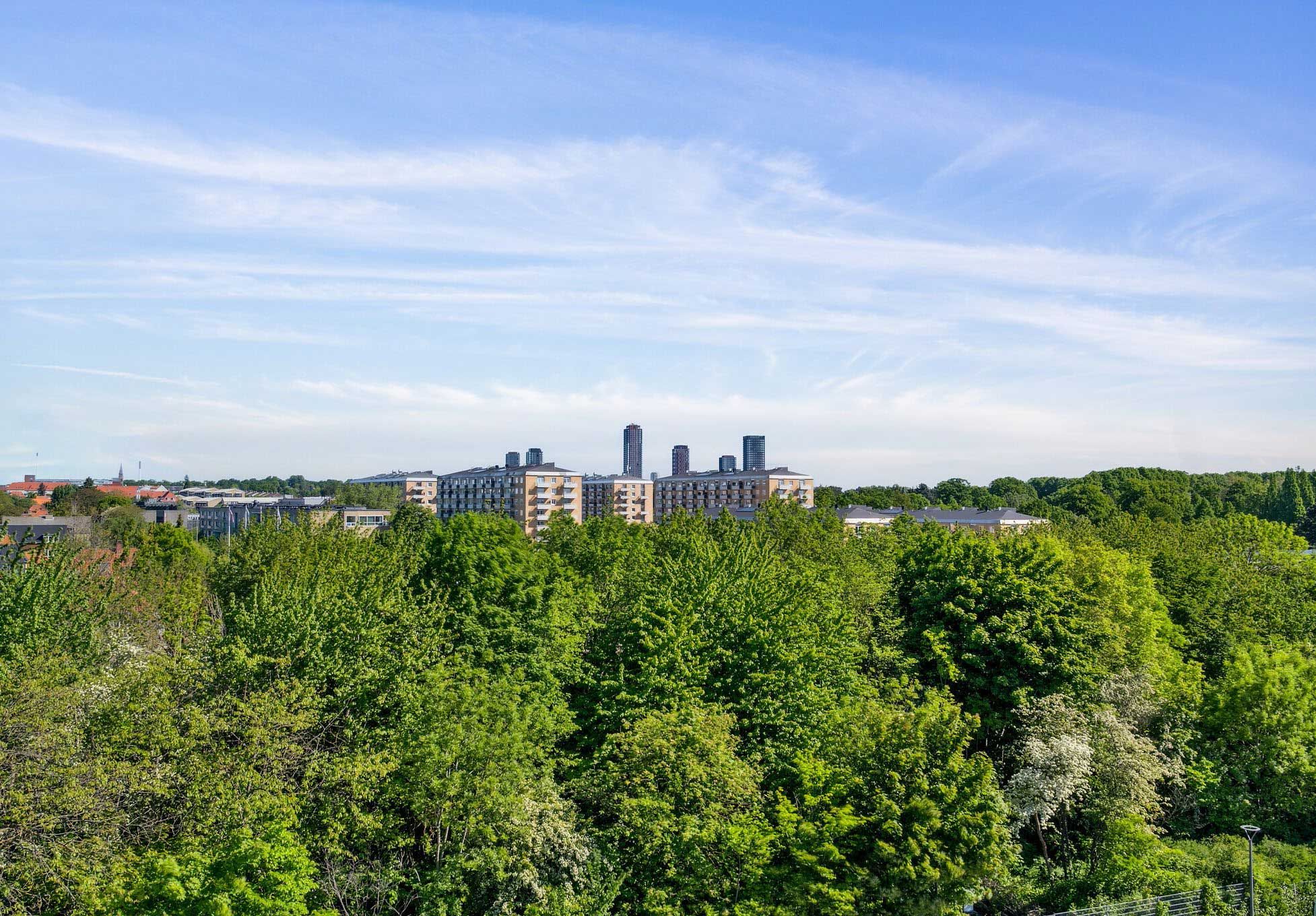 Panorama over byen København SV med moderne bygninger, tætte grønne træer og en klar, blå himmel med hvide skyer