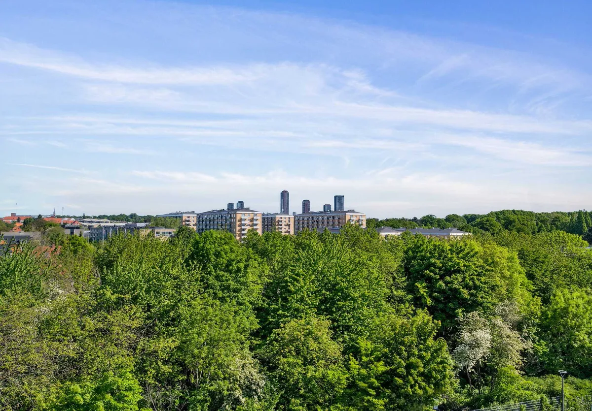 Panorama over byen København SV med moderne bygninger, tætte grønne træer og en klar, blå himmel med hvide skyer