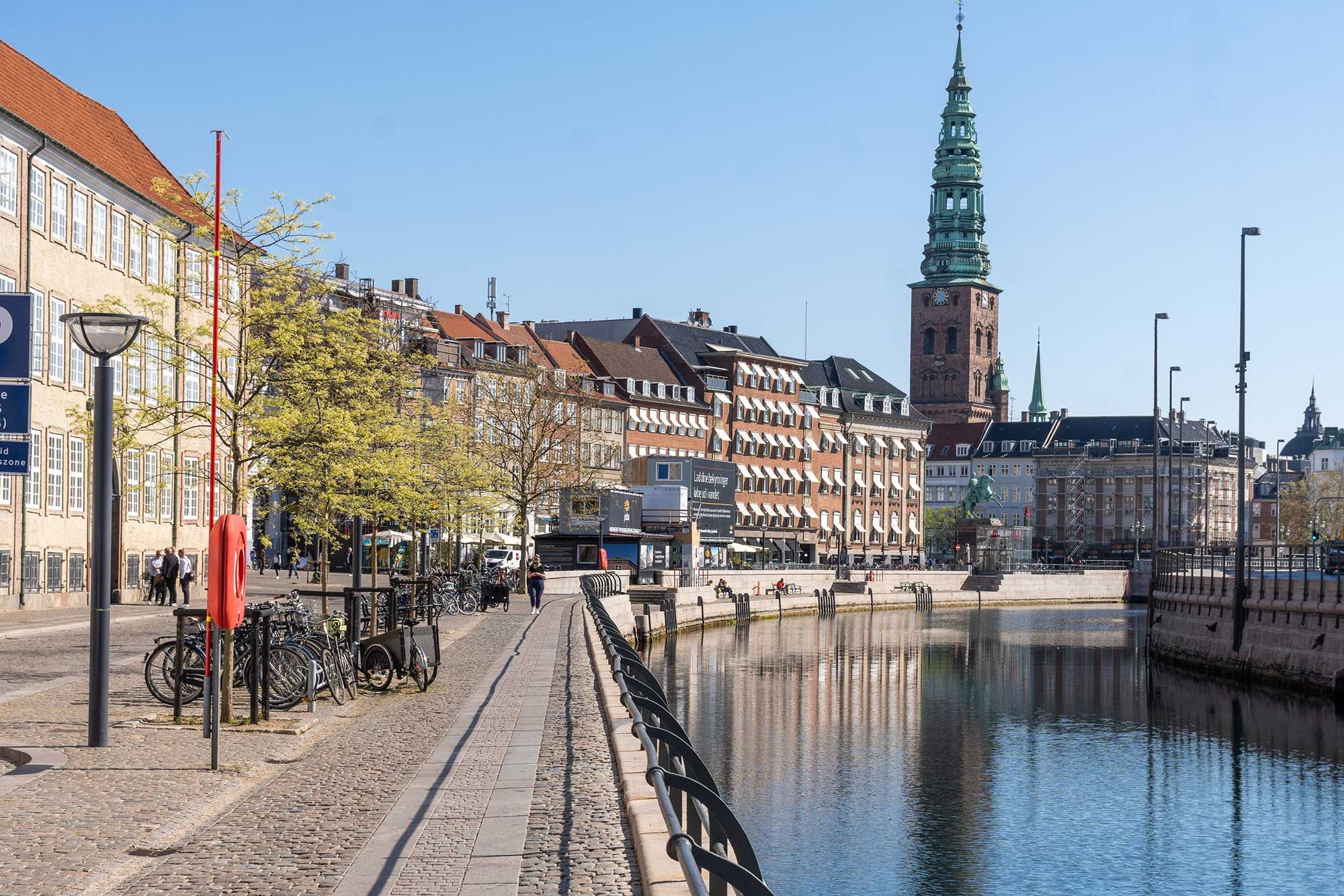 Lejlighed til leje i Kompagnistræde. Gammel Strand med bygninger og sø. Mennesker og cykler parkeret. Lys og luftige baggård med grønne træer og sø.