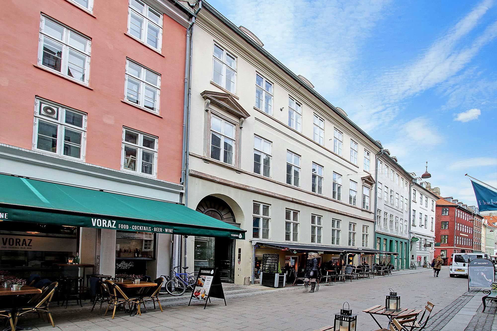 Baggård med flere bygninger og et café med navnet Voraz, hvor der er flere borde og stole uden for og et flag hænger på en bygning