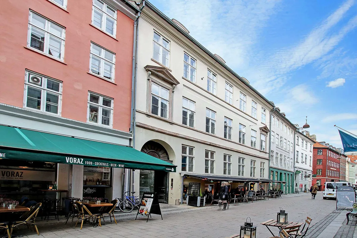Baggård med flere bygninger og et café med navnet Voraz, hvor der er flere borde og stole uden for og et flag hænger på en bygning