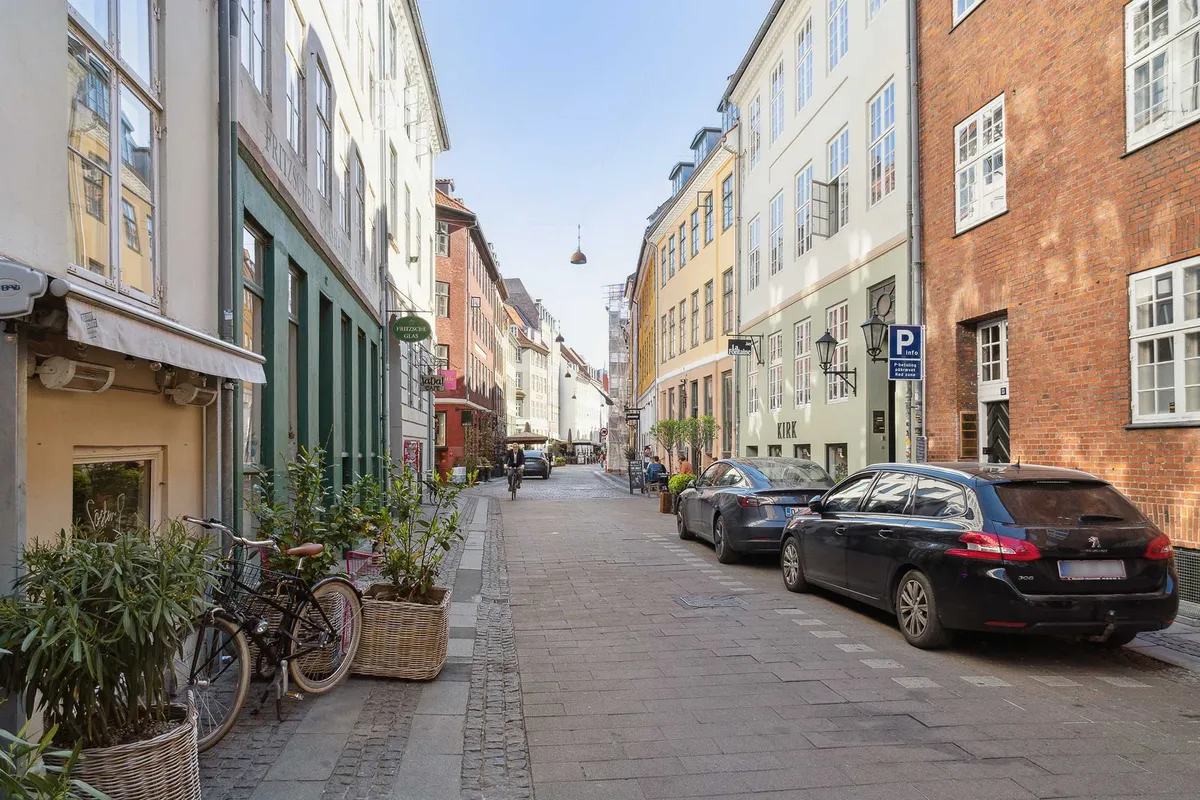 Kompagnistræde, København med to parkerede biler, cykel, buske, vinduer og facader med røde mursten og grønne ruder.