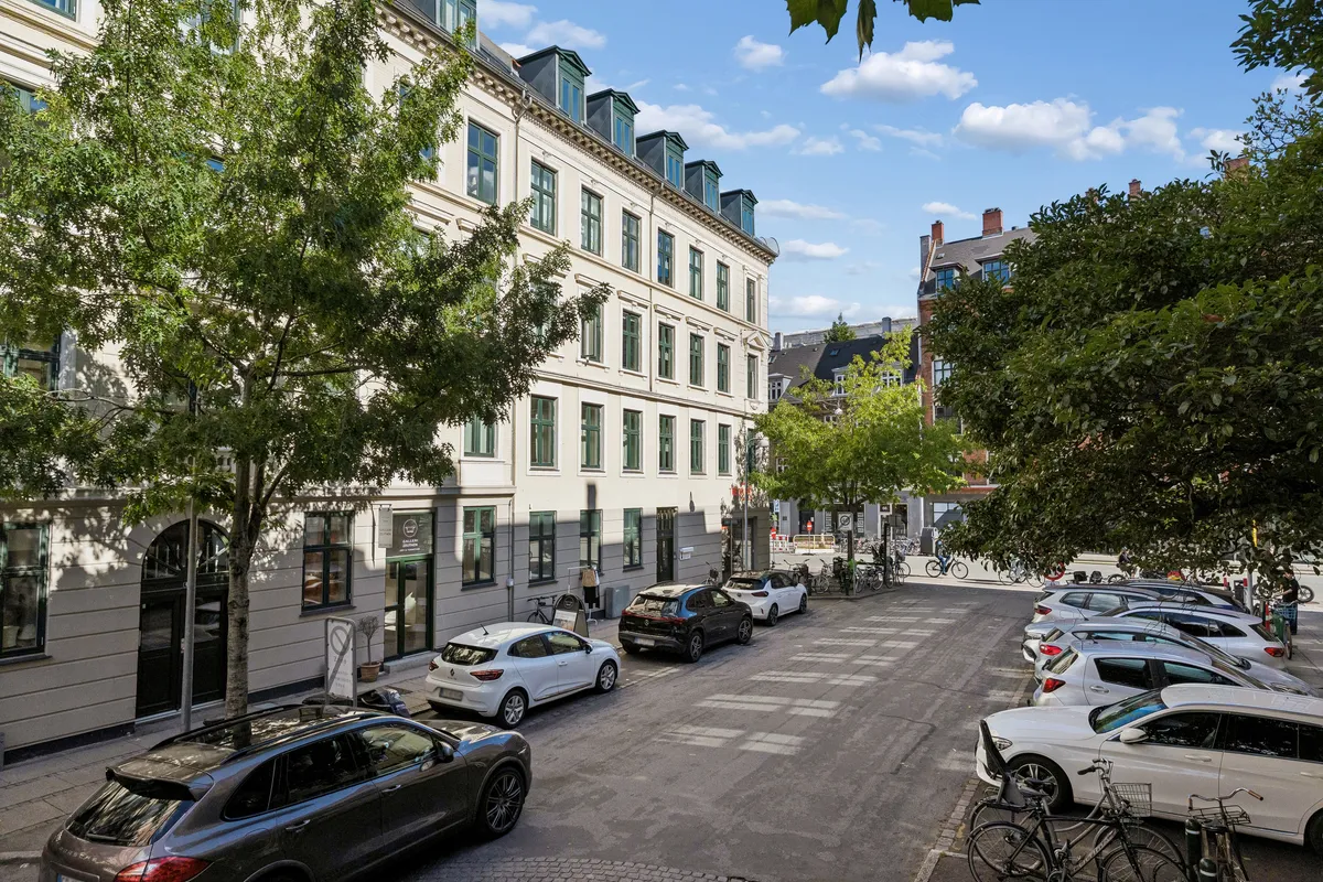 Lejlighed i Frederiksberg med høj loftshøjde og lyse vinduer, parkerede biler og træer langs gaden