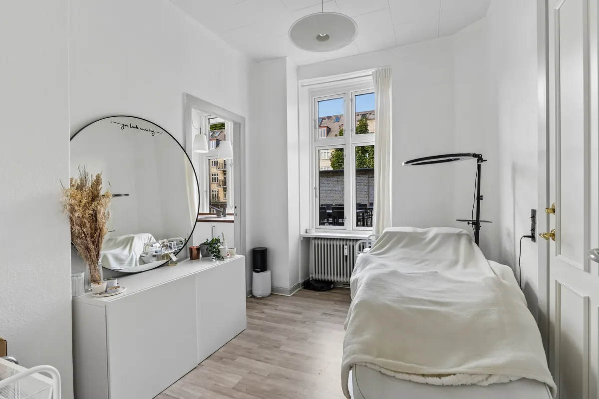 Luksuriøs kontor med høj loftshøjde, vinduer med udsigt til grønne områder, en stor rundspejl, et hvidt bord med dekorationer, et højt stativ og en lampe