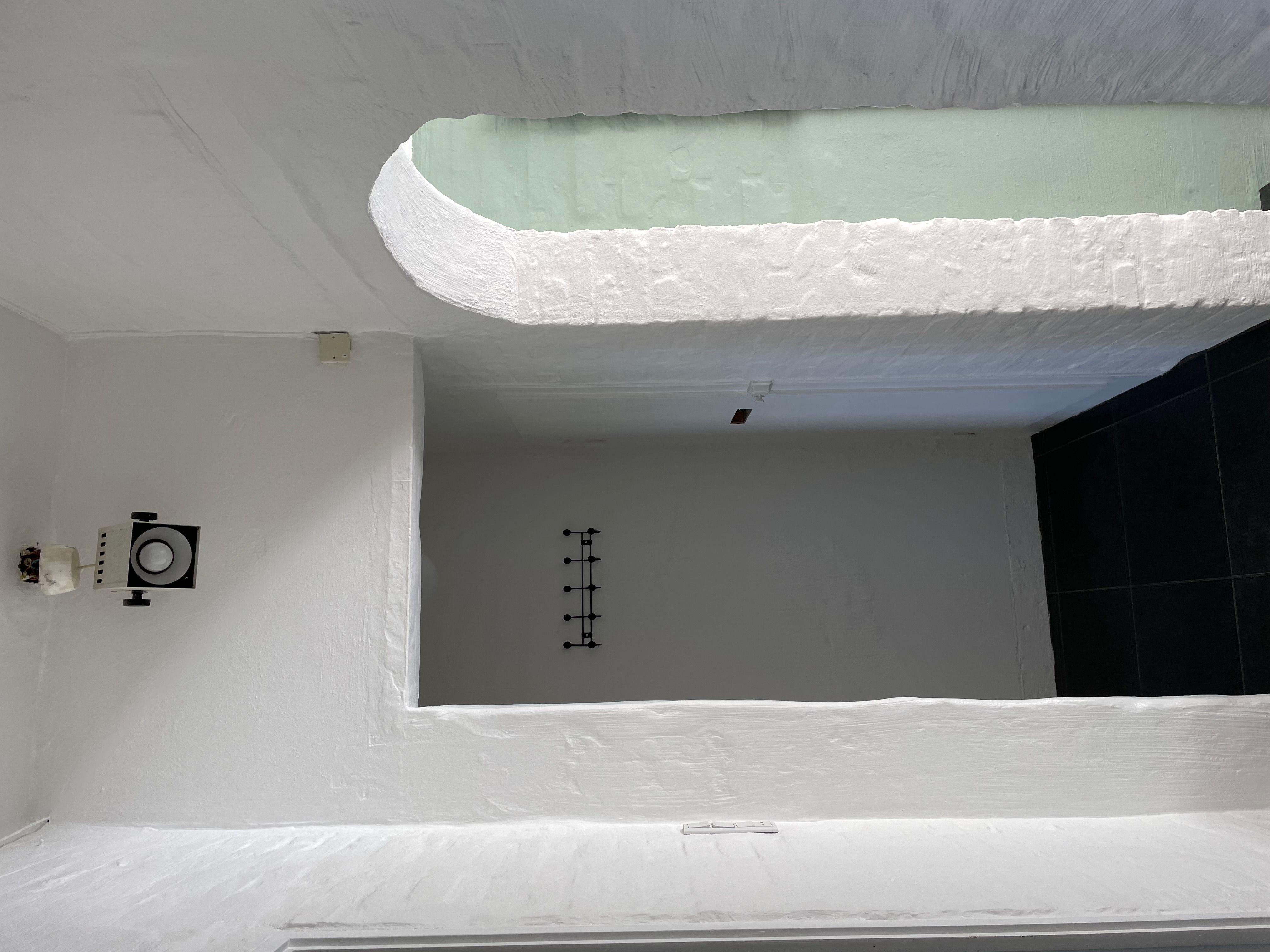 Minimalistisk hvid malet værelse med en bueformet åbning og en slank sort væghængende. Sort gulv og loft med en hvid ramme og en hvid højttaler.