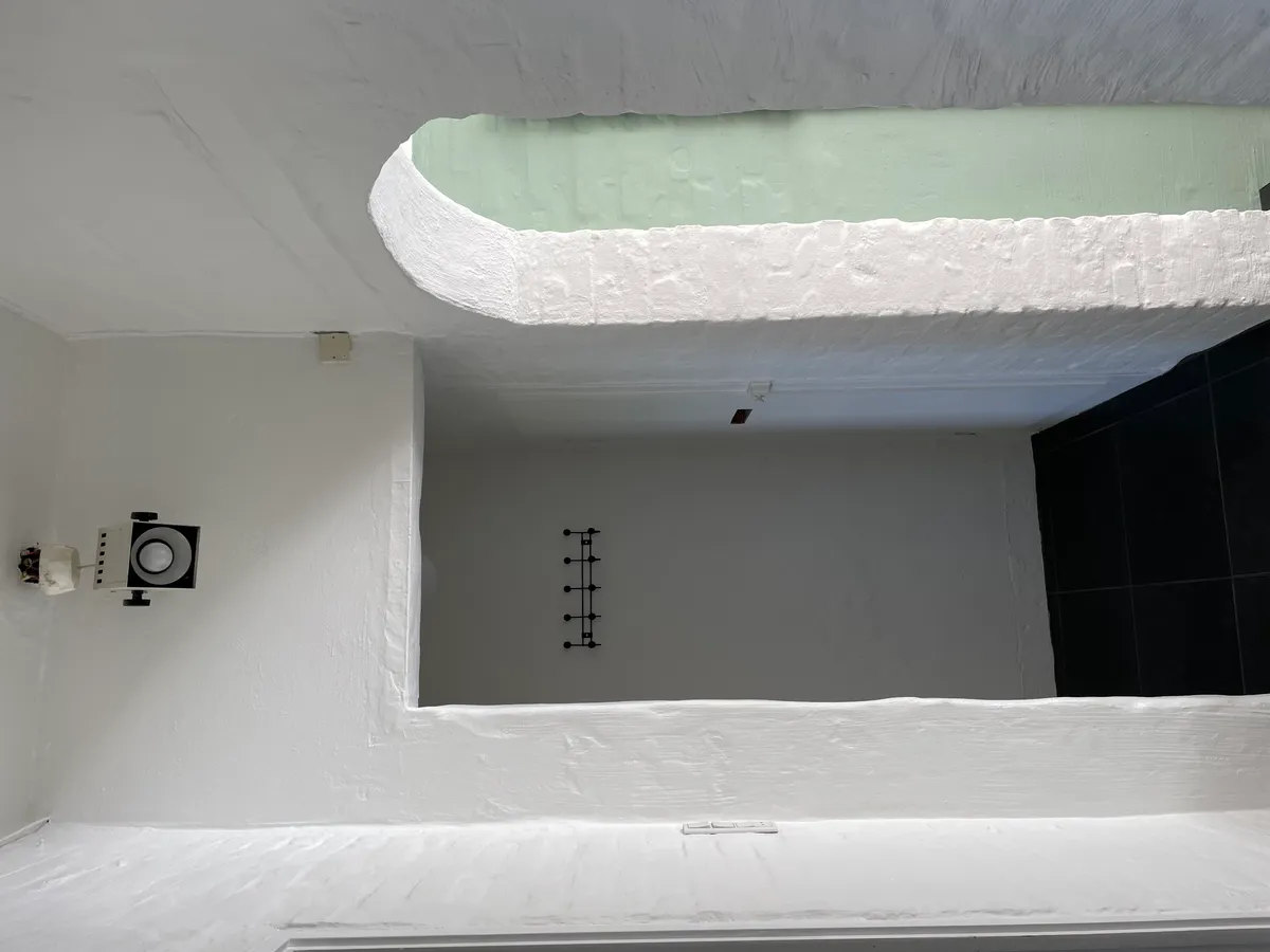 Minimalistisk hvid malet værelse med en bueformet åbning og en slank sort væghængende. Sort gulv og loft med en hvid ramme og en hvid højttaler.