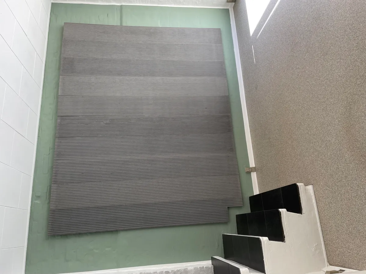 Stairs og grøn væg med gulvbelægning i stribet træmateriale. To stribede gulvbelægningsplader ligger på væggen og er ikke endnu monteret