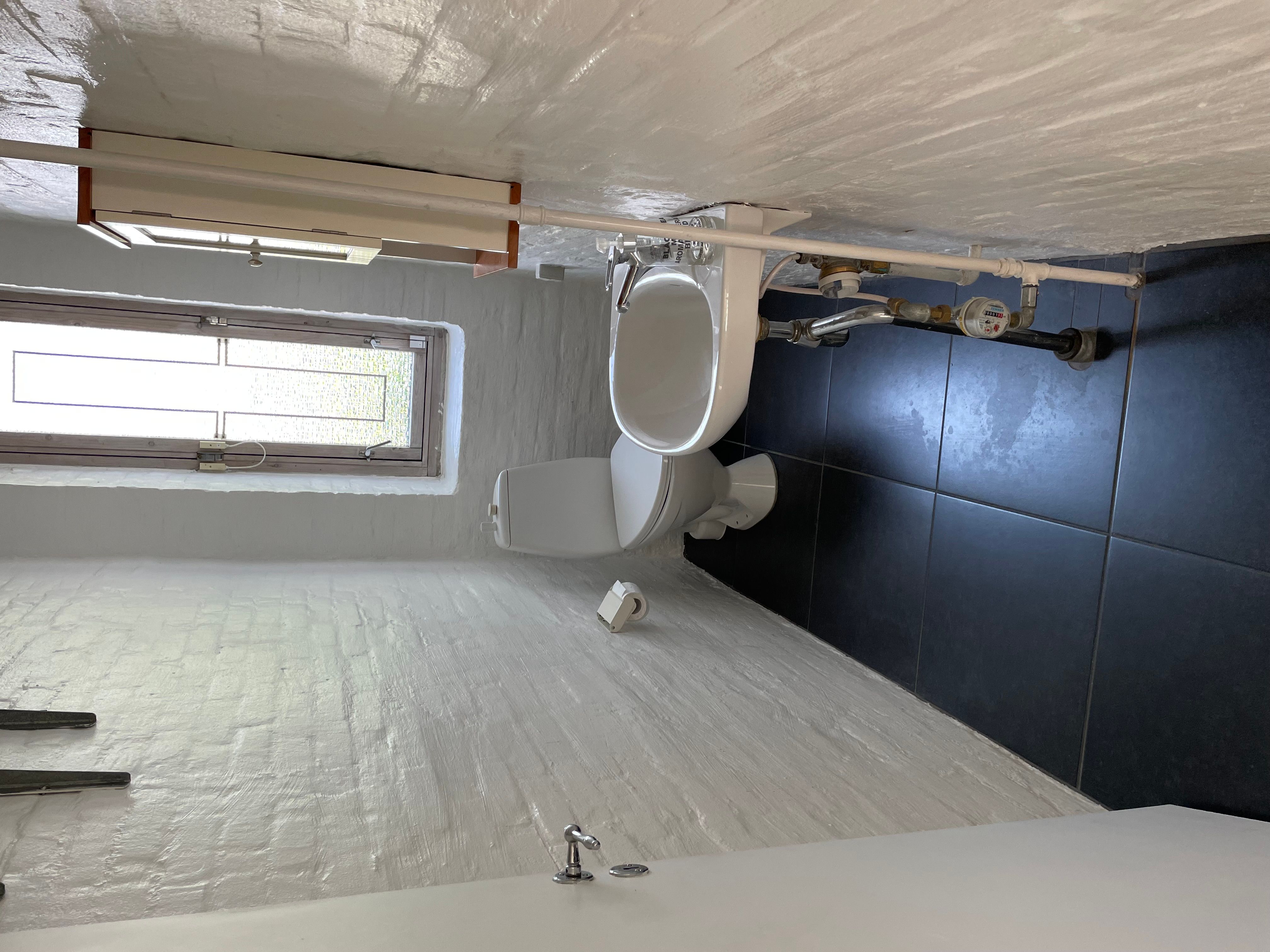Badeværelse med toilet, toiletpapir, vindue, hvid og sort flise og tørretumbler på loftet
