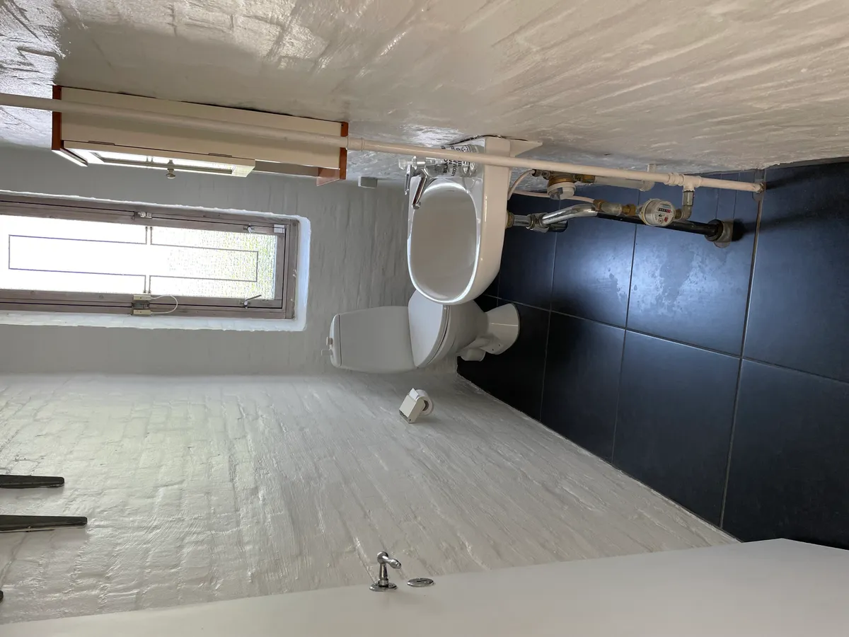 Badeværelse med toilet, toiletpapir, vindue, hvid og sort flise og tørretumbler på loftet