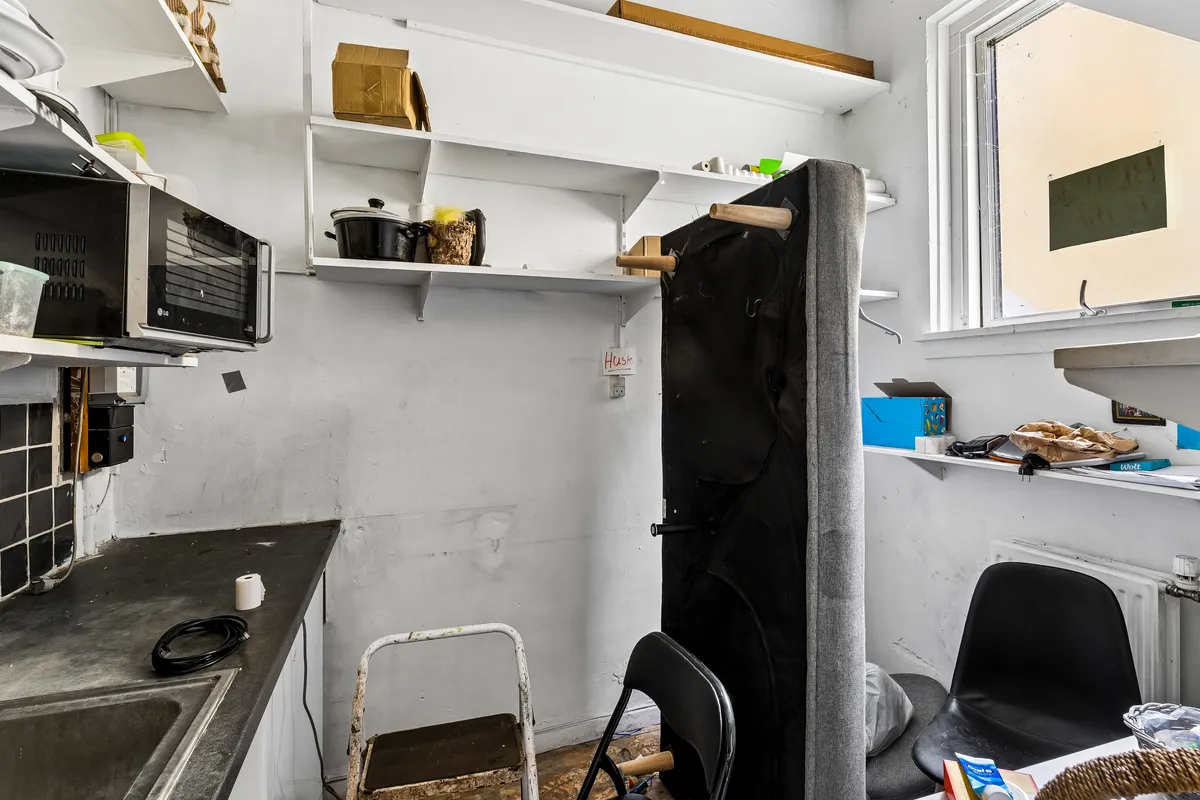 Køkken med mikroovn og højrekantet bord, en stol og en sofa med stofbetrækning og radiator under vinduet.